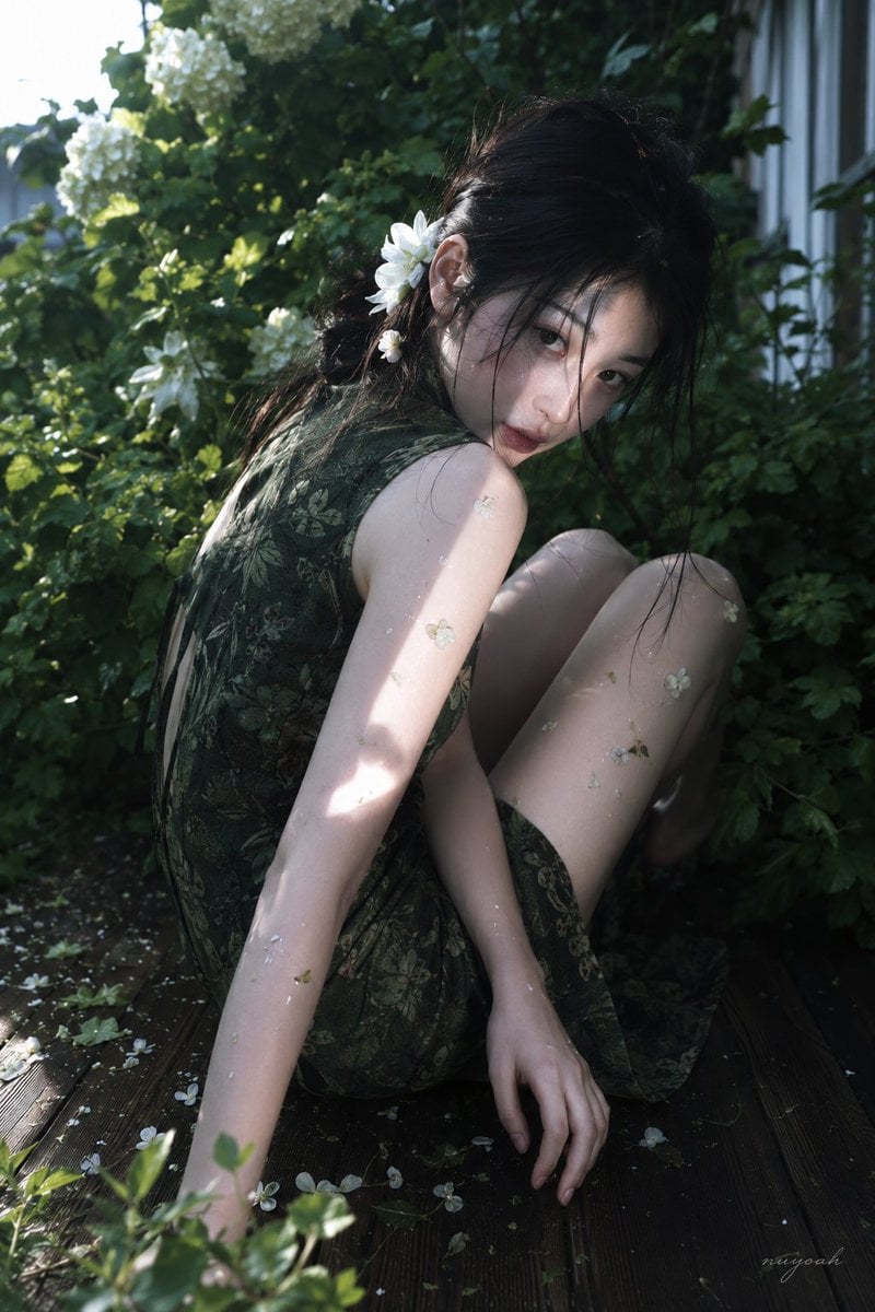 真人摄影，真实人物，户外花园唯美人像写真，低饱和冷绿调与斑驳自然光，轻微胶片柔焦和电影感。竖幅近中景，略高机位俯拍，人物占画面约70%，身体斜…