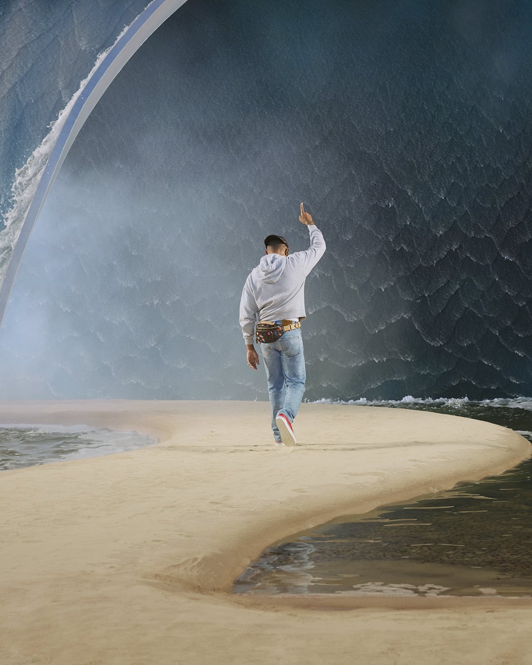 A man walking on a sandy path towards a massive artificial wave, part o…