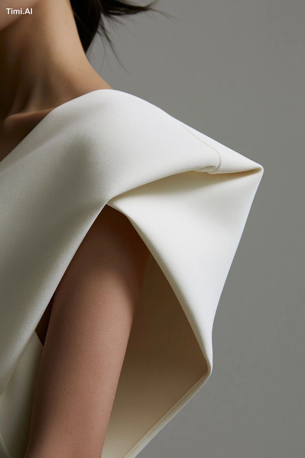 A close-up of a strong structural shoulder fold in a chalk-white crepe …