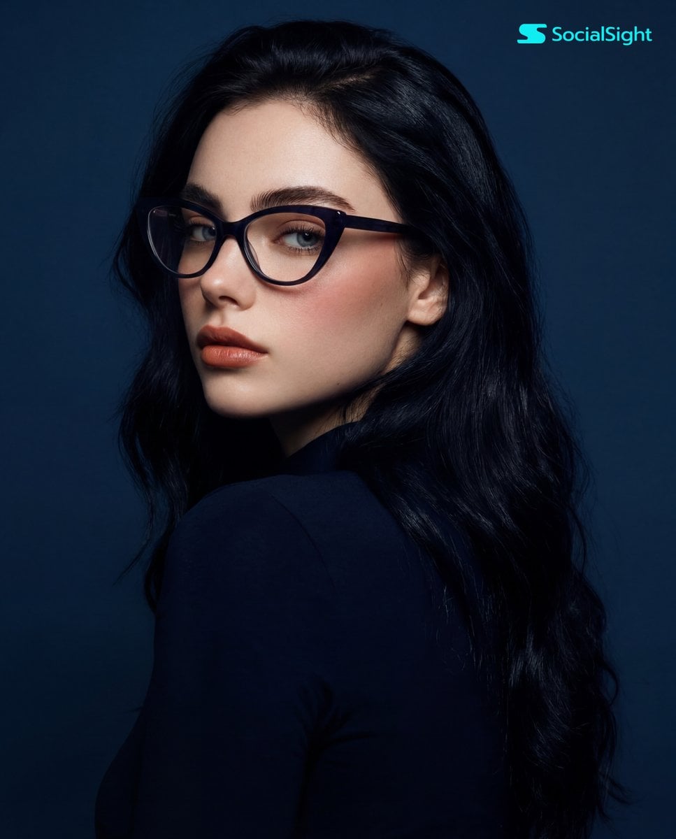 A young woman with long, dark hair and striking cat-eye glasses is capt…