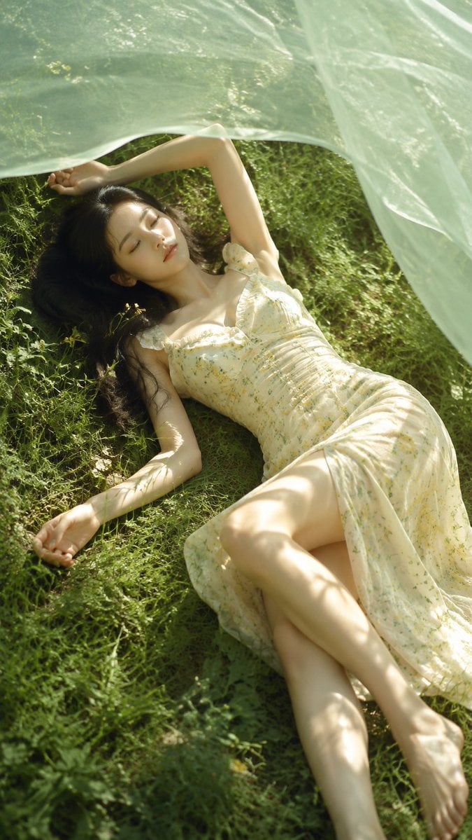 A realistic outdoor natural-light portrait of an adult young woman lyin…