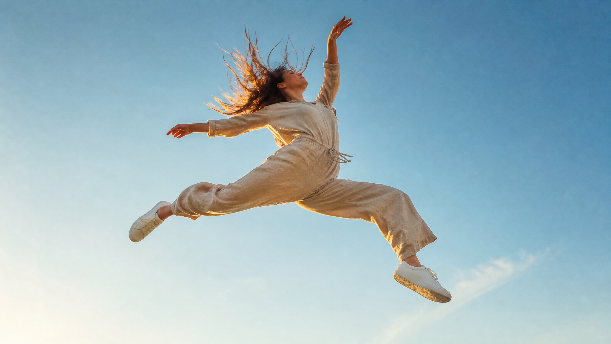 A young woman captured mid-air in a dynamic, gravity-defying leap, her …