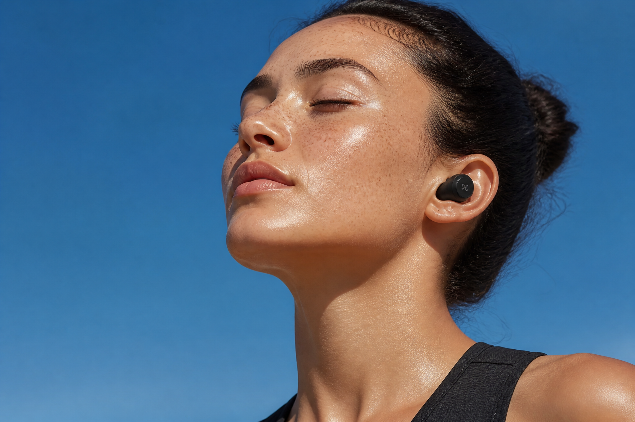 A serene close-up of a freckled woman with wireless earbuds, eyes close…
