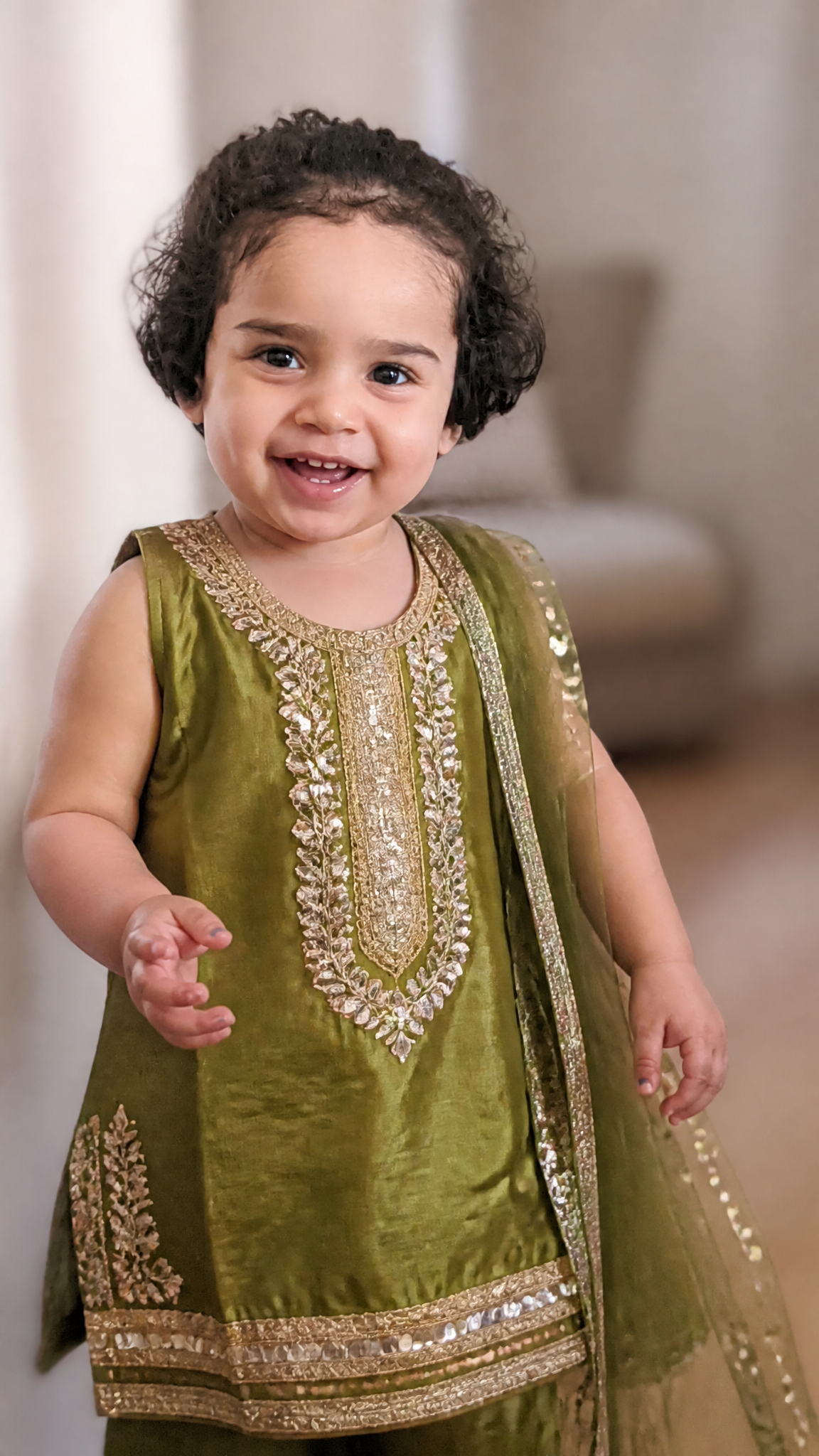 A joyful toddler stands in a brightly lit indoor space, wearing a vibra…